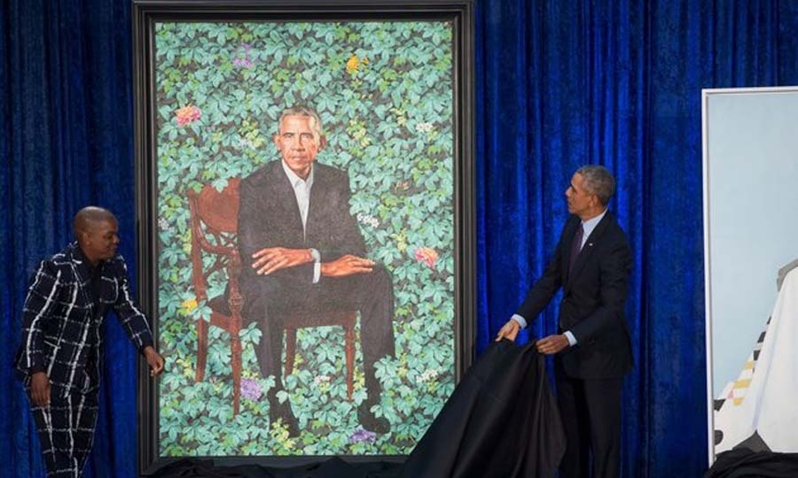 Ο Barack Obama κάθεται σε μια ξύλινη καρέκλα με φόντο έναν κήπο με πολύχρωμα λουλούδια