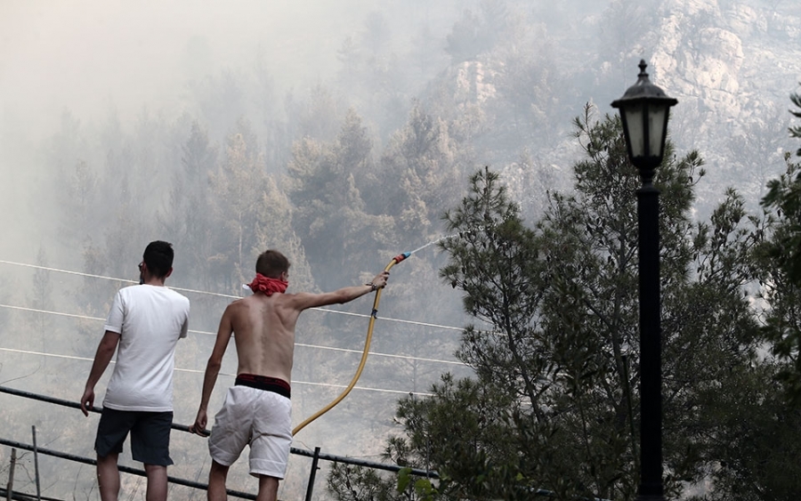 Kάτοικοι και απλοί εθελοντές προσπαθούν να σβήσουν τις φλόγες με κουβάδες και λάστιχα.